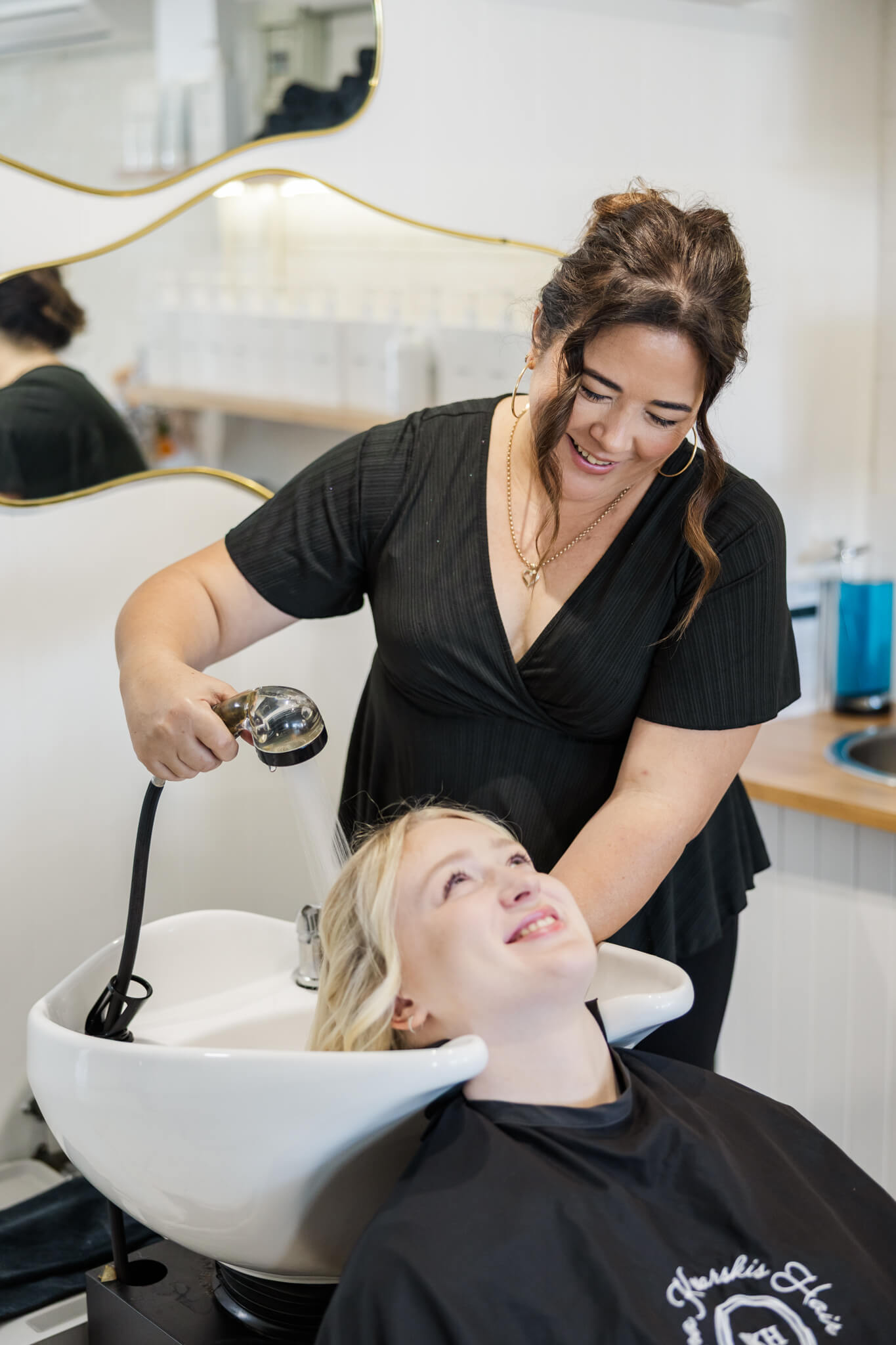 A hairdresser washing client's hair at a basin.