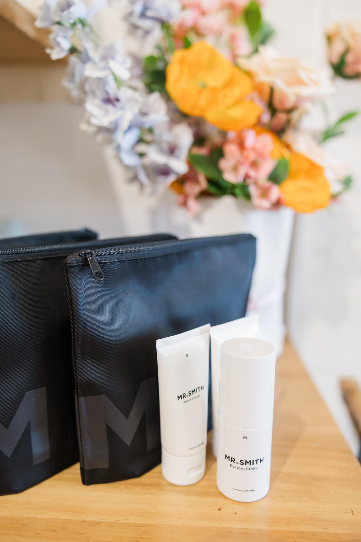 A bunch of flowers next to a make up bag and some hair product containers.